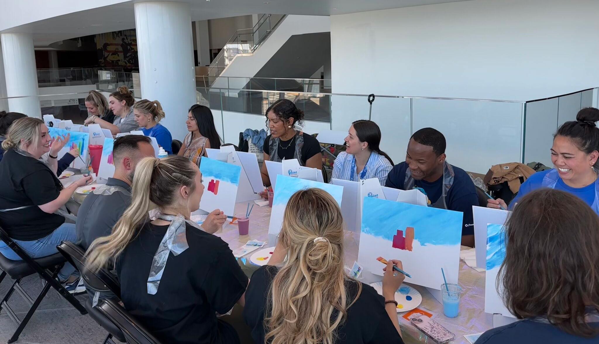 Employees sitting at a long table participating in an oil painting class.