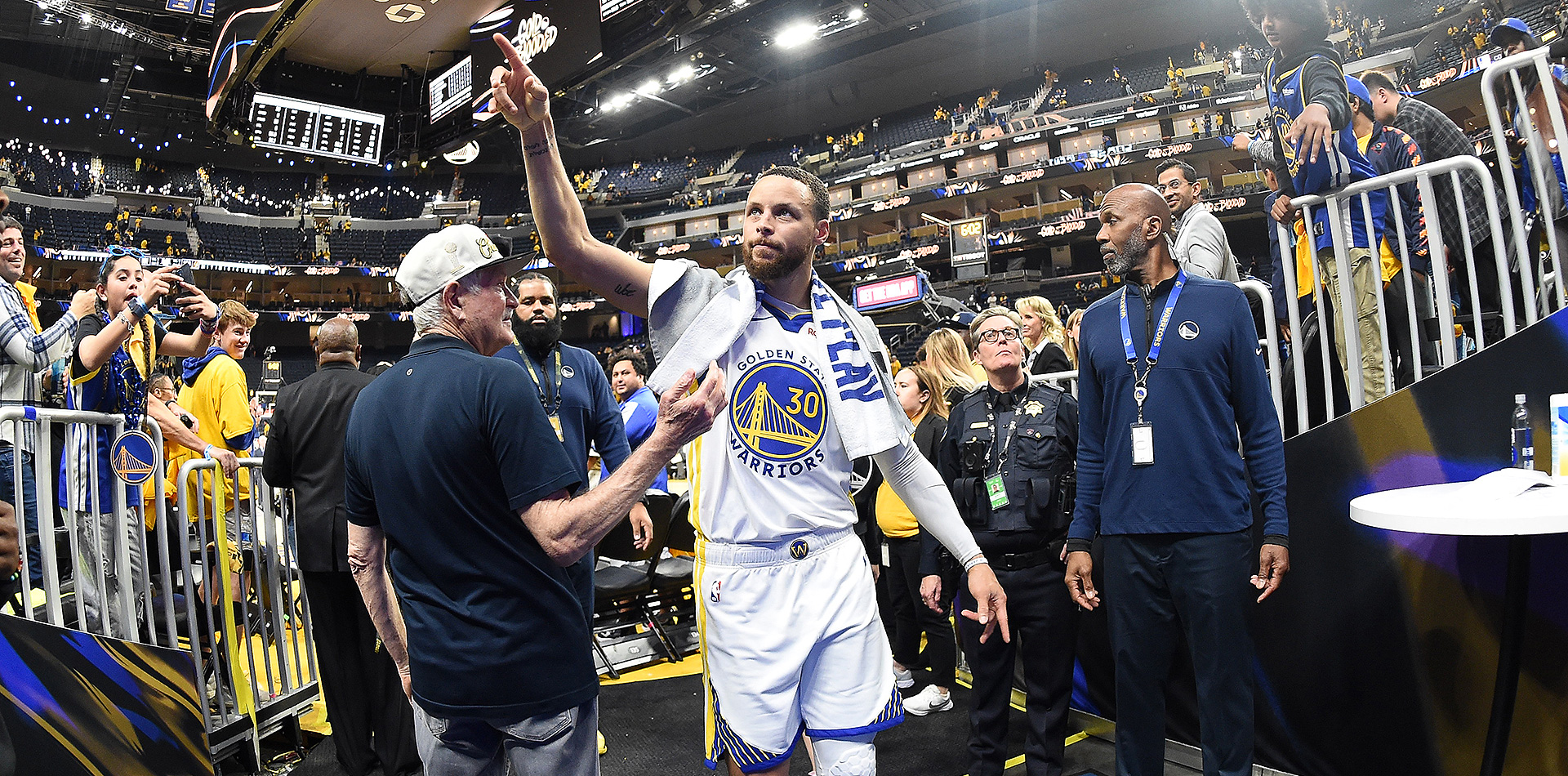 Steph Curry walking off of the court while fans take pictures of him.