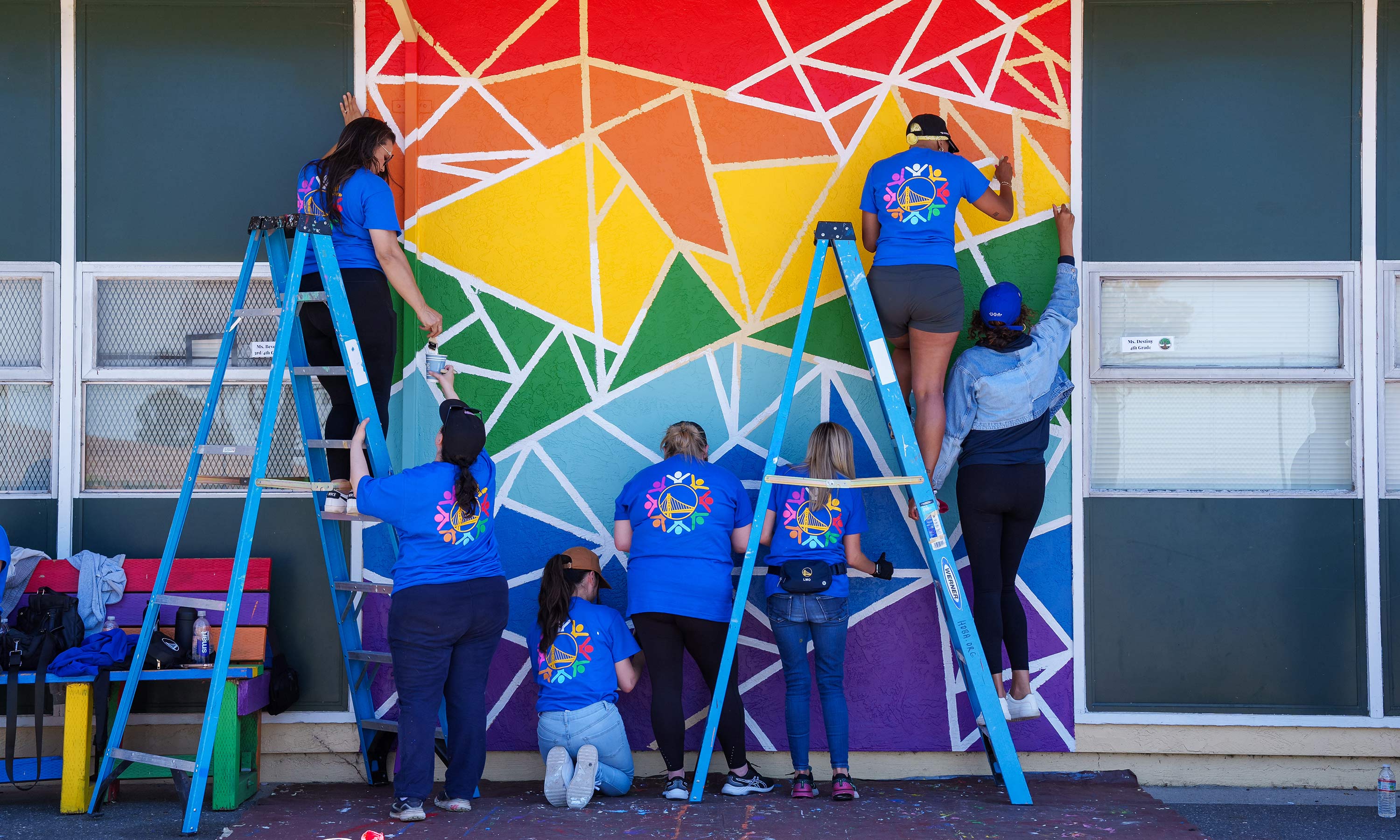 Employees painting a mural outside on the side of a building.