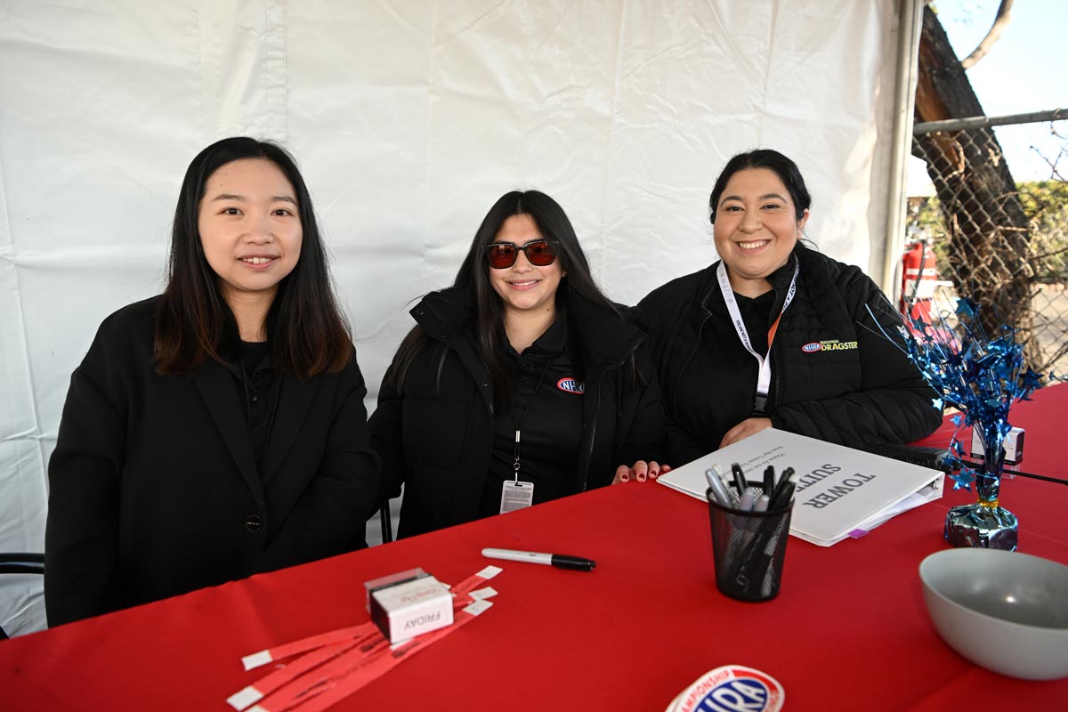 Three women sitting at an NHRA outside booth
