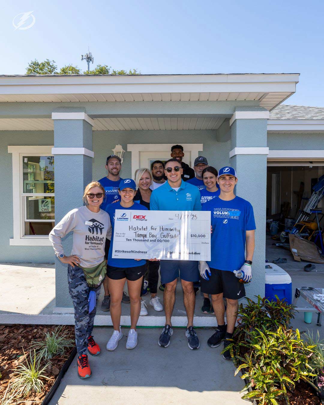 A group of employees in front of a house holding up a large check that signifies a donation of $10,000 from the Tampa Bay Lightning to Habitat for Humanity