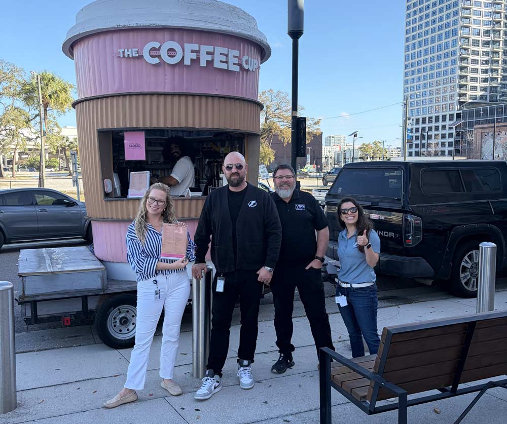 Four young adults in front of a coffee shop on the sidewalk that is built in the shape of a coffee cup