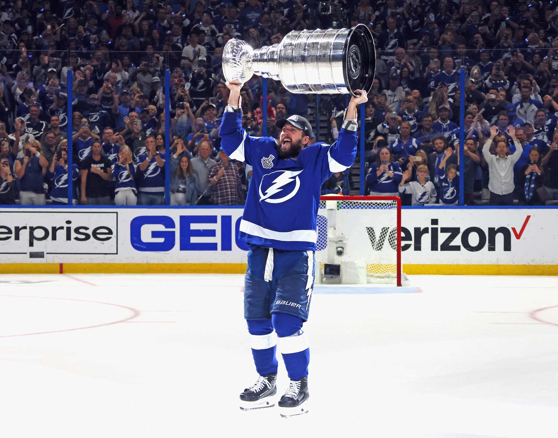 A Tampa Bay Lightning hockey player holding up the Stanley Cup trophy on the ice of the arena