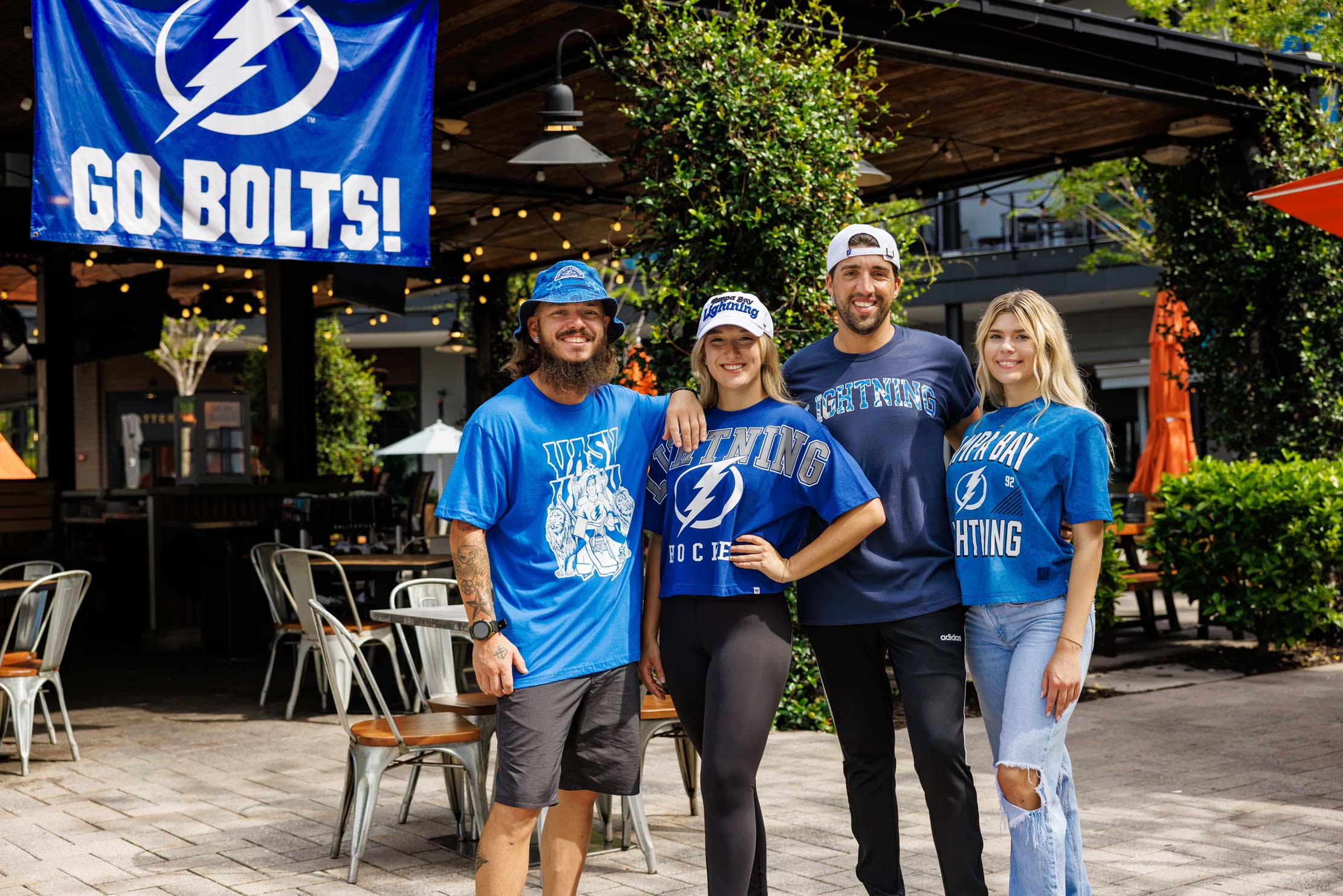 2 men and 2 women sports fansstanding in front of an outdoors restaurant wearing Tampa Bay Lightning jerseys and t-shirts
